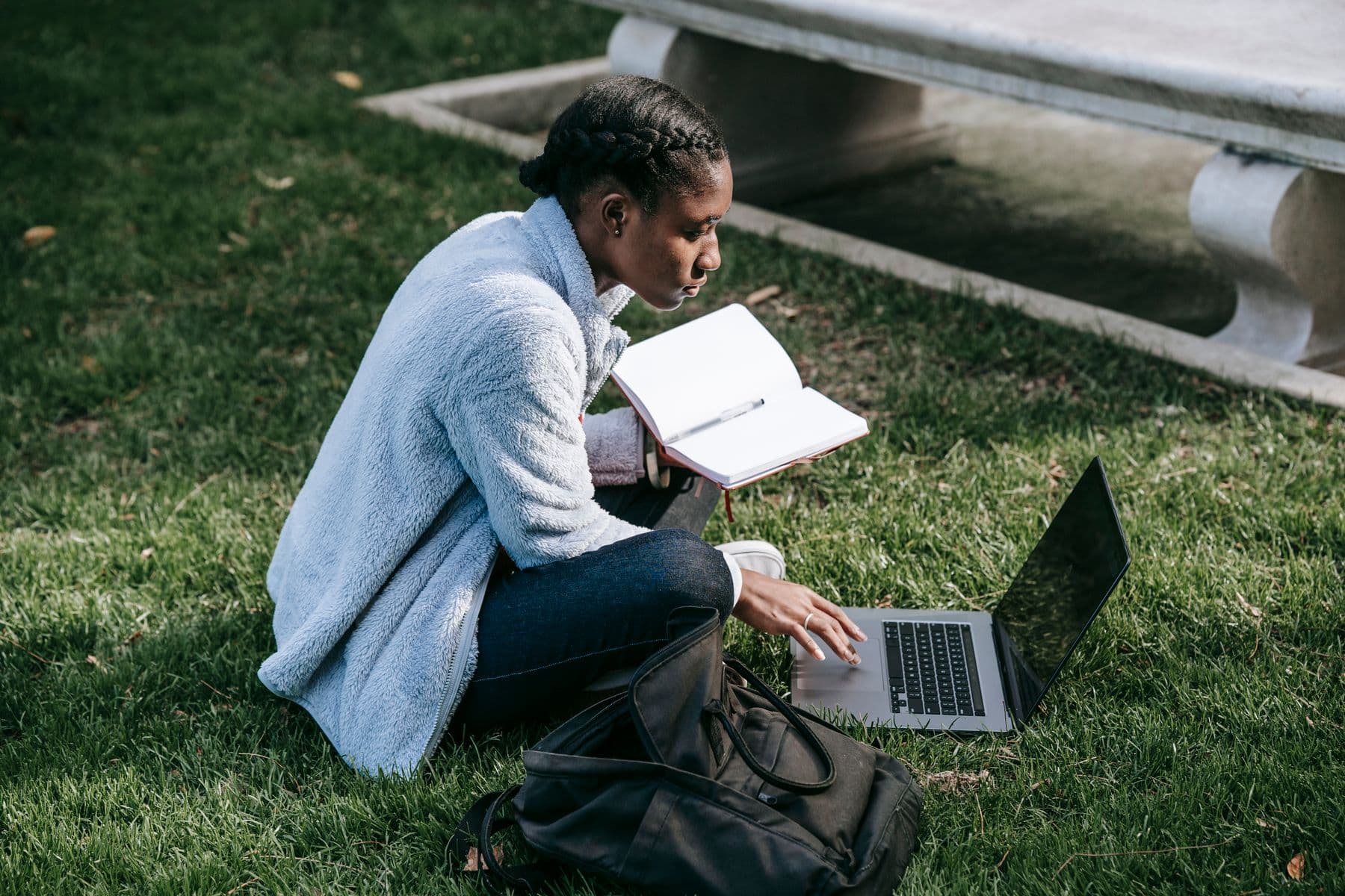 A student researching outside with a notebook and laptop