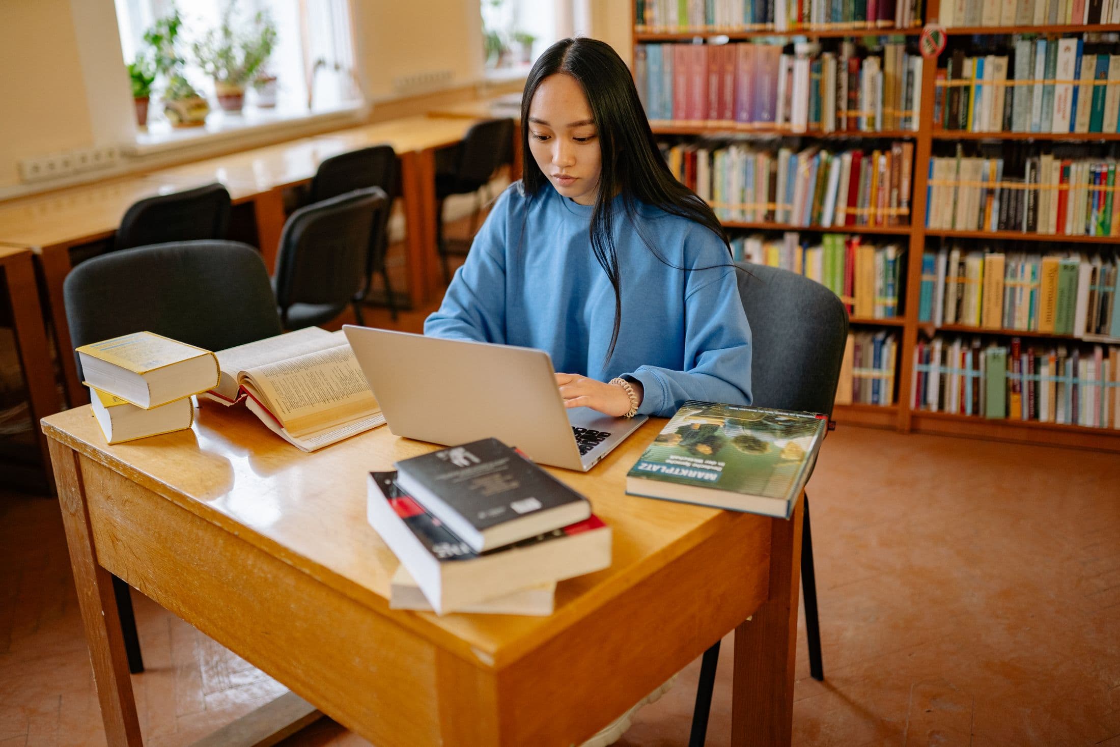 A student researching with a laptop and books in a library